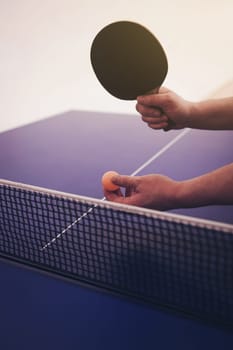 man is playing ping pong. He holds a ball and a racket in his hands