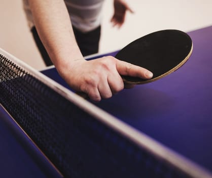 player's hand with a tennis racket on a blue table background. ping pong game