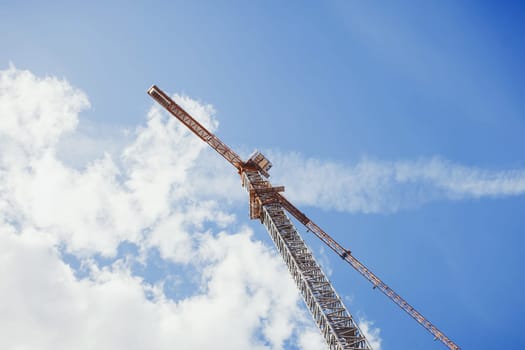 perspective view looking up tall construction crane on a building site against a blue sky
