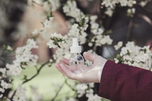 Hand sanitizer dispenser, infection control concept. Sanitizer to prevent Coronavirus or Covid-19, flu. Spray bottle. Alcohol spray on blooming trees background
