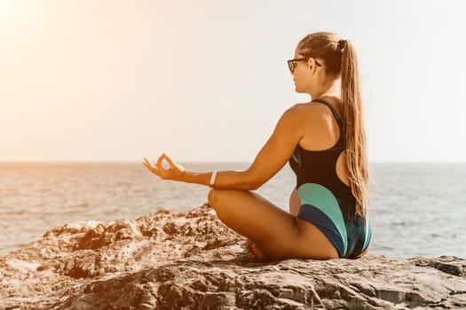 Yoga on the beach. A happy woman meditating in a yoga pose on the beach, surrounded by the ocean and rock mountains, promoting a healthy lifestyle outdoors in nature, and inspiring fitness concept