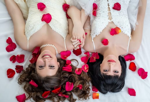 Top view of two charming brides looking at camera while lying on bed