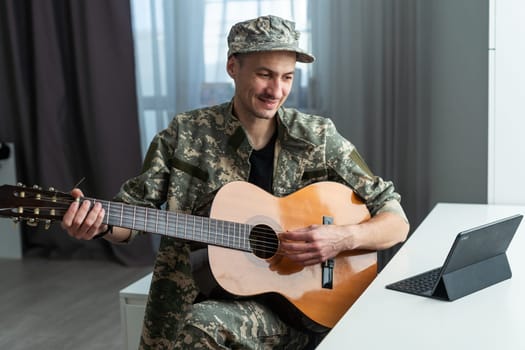 Cheerful smiling young military man wearing khaki uniform holding guitar. High quality photo