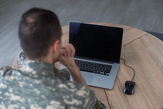 Young hispanic man army soldier using laptop sitting on table at home. High quality photo
