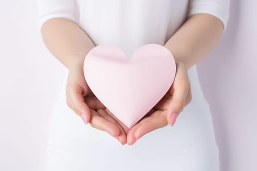 A gentle pink paper heart in the hands of a girl.