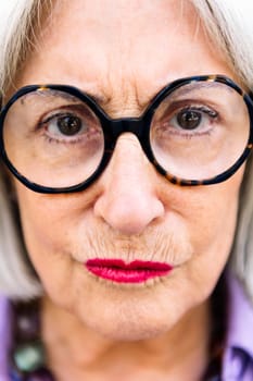 close-up portrait of senior woman pressing lips and looking at camera, concept of elderly people and active lifestyle