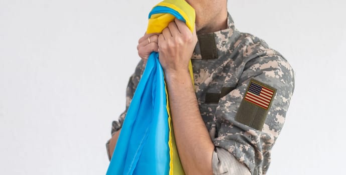 American Flag on Soldiers arm and flag of the Ukraine at background. US military support Ukraine.