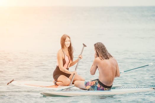 Sea woman and man on sup. Silhouette of happy young woman and man, surfing on SUP board, confident paddling through water surface. Idyllic sunset. Active lifestyle at sea or river