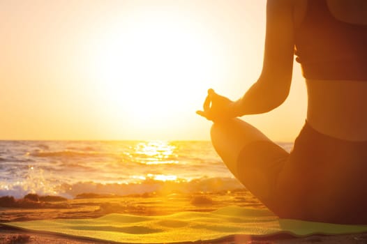 Close-up Yoga woman meditating at serene sunset or sunrise on the beach. The girl relaxes in the lotus position. Fingers folded in mudras
