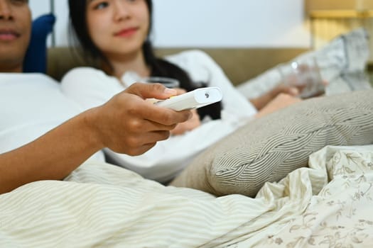 Cropped shot of man holding remote control watching movie with his wife in bedroom.