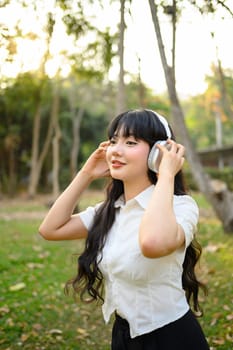 Attractive girl listening to favorite audio tracks with headphones and relaxing in nature.