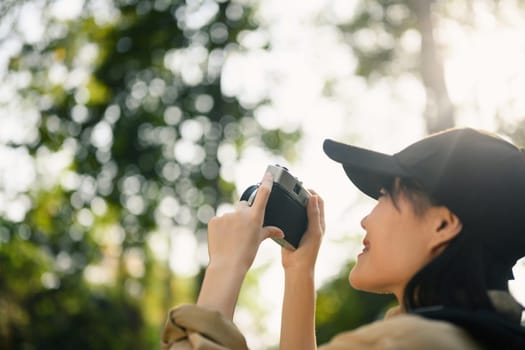 Happy young woman trekking among trees and taking pictures with vintage camera.