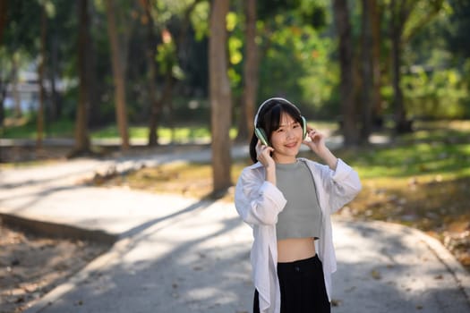 Pleased young woman enjoy leisure time and listening the music with headphone in the public park.