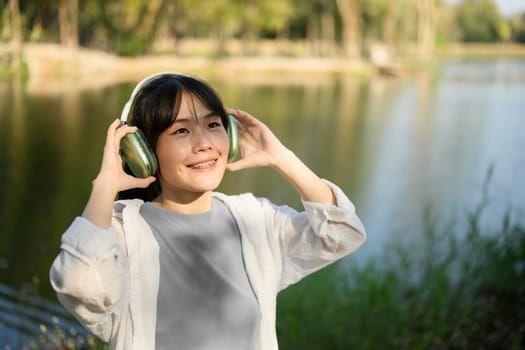 Attractive serene woman listening to music in headphones near a forest lake.