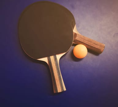 Two table tennis or ping pong rackets and ball on a blue table with net background

