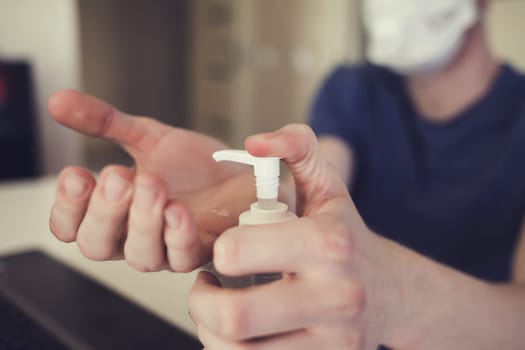 man in a mask at home puts an antibacterial gel on his hands