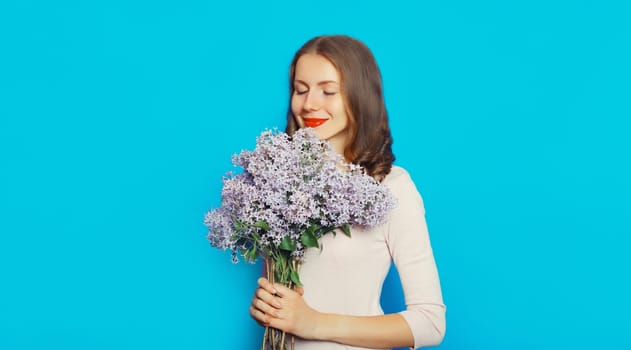 Portrait of beautiful happy smiling woman with bouquet of fresh lilac flowers, wildflowers on blue background