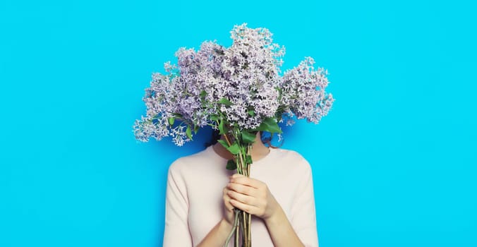 Portrait of woman covering her head with bouquet of fresh lilac flowers on blue background