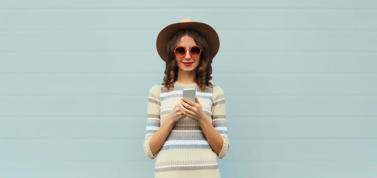 Portrait of stylish young woman with smartphone in round hat, sunglasses on gray background
