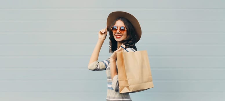 Stylish beautiful happy smiling young woman posing with shopping bags in round hat, dress on gray background