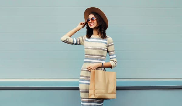 Stylish beautiful happy smiling young woman posing with shopping bags in round hat, dress on city street