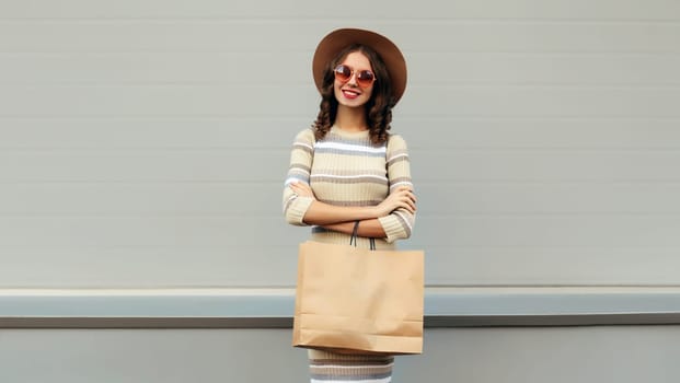 Stylish beautiful happy smiling young woman posing with shopping bags in round hat, dress on city street