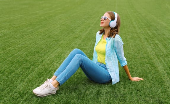 Portrait of happy smiling young woman listening to music in headphones while lying on grass in summer park