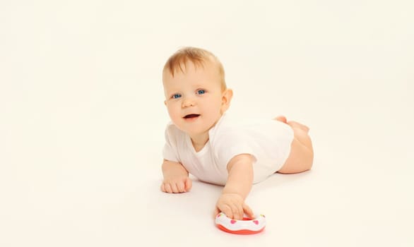 Happy little baby playing with toys while sitting on floor on white studio background