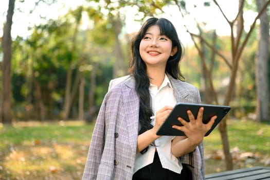 Shot of confident businesswoman holding digital tablet and looking away sitting in park.