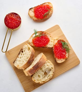 Red caviar on slices of white wheat bread on a white table, concept of luxury and gourmet cuisine