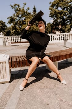 Stylish woman in the city. Fashion photo of a beautiful model in an elegant black dress posing against the backdrop of a building on a city street.