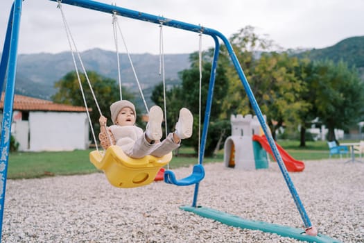 Little girl swings on a rope swing on a playground in a green park. High quality photo