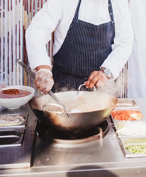 Chef stirs vegetables and noodles in wok