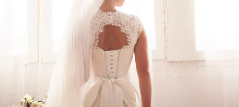 Beautiful bride on room background. On the woman in wedding dress with lace and an open back