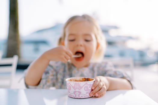 Little girl eats ice cream with a spoon, holding a cup with her hand. Blur. High quality photo