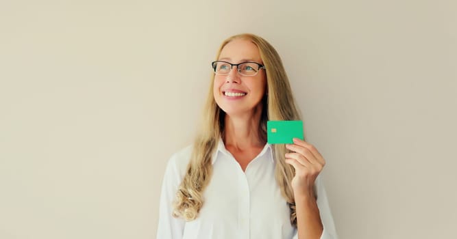Portrait of happy successful smiling middle-aged woman holding plastic credit bank card on studio white background