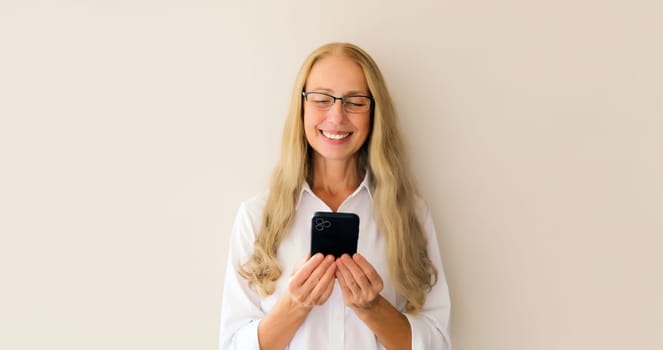Portrait of happy smiling middle-aged woman with mobile phone looking at device on white studio background