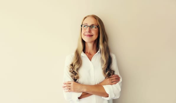 Portrait of happy smiling caucasian middle aged woman employee manager looking away in eyeglasses with crossed arms on white studio background