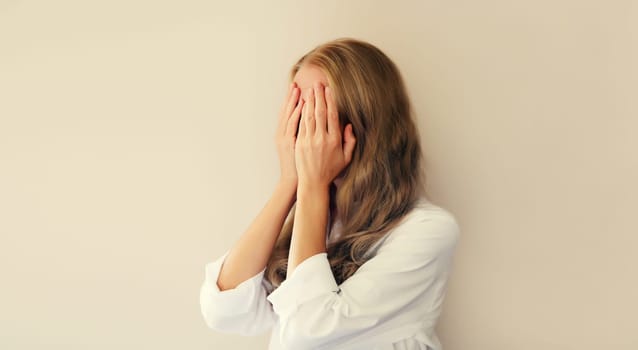 Upset sad crying woman covering her eyes and face with hands while experiencing mental or physical suffering on studio background