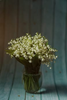 A small bouquet of lilies of the valley in vase on wooden background