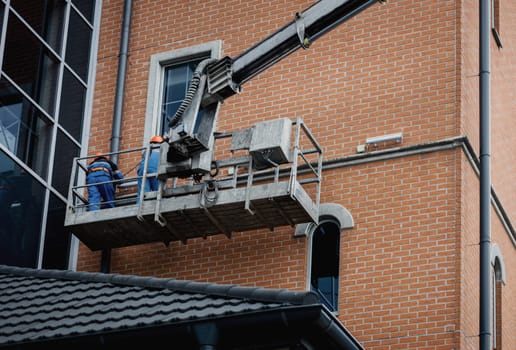 Workers in hardhat repair facade of the building at height in lifting cradle. Finishing facade work.