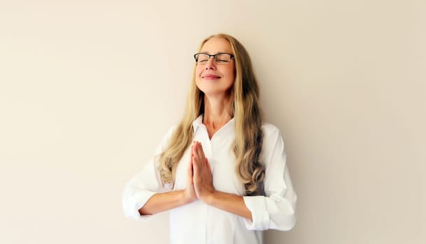 Calm relaxing healthy middle-aged woman meditates, practicing yoga on white studio background