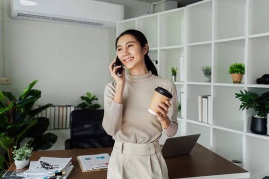 Businesswoman hold an eco-friendly paper coffee cup and talk on mobile in nice office environment.