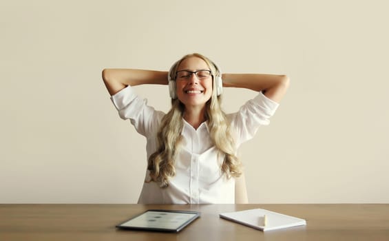 Happy relaxing middle aged woman listening to music in headphones working with digital tablet computer sitting at desk at home