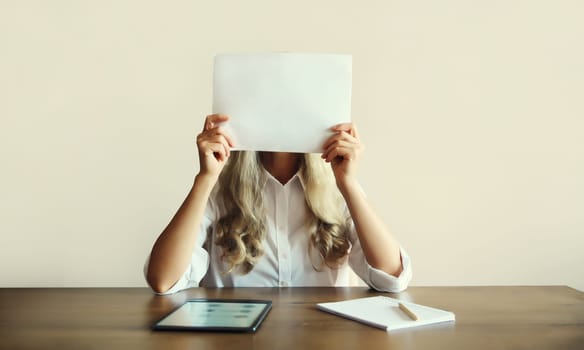 Woman showing and holding white blank sheet of paper document for text copy space while working with digital tablet computer sitting at the desk