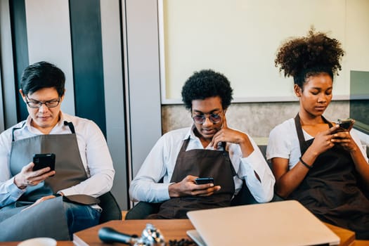 Barista team in a cafe diverse group looking at smartphones relaxing together. Professionals in uniform enjoying a moment while connected through phones. Teamwork in a cafe setting. No order