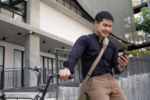 A young Asian businessman rides a bicycle to work. Standing outside the office talking on the phone and talking about business. Concept of reducing energy and reducing air pollution..