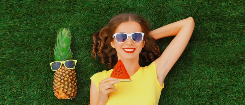 Summer portrait of happy smiling young relaxing woman with fruits, pineapple in sunglasses lying on green grass in the park