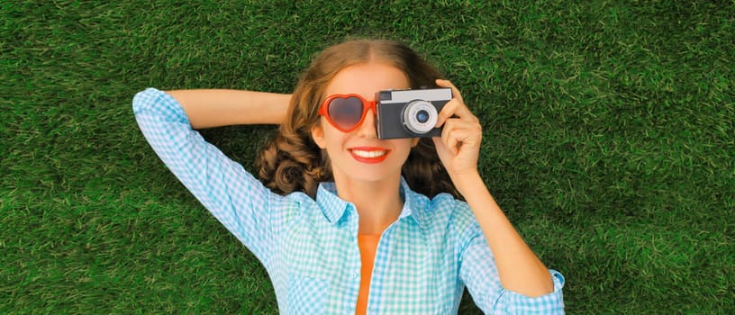 Summer portrait of happy smiling young woman photographer taking pictures on camera lying on green grass in the park