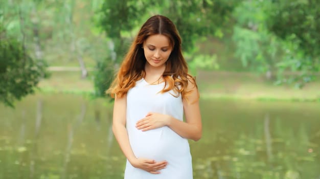 Portrait of beautiful happy young pregnant woman walking in summer park